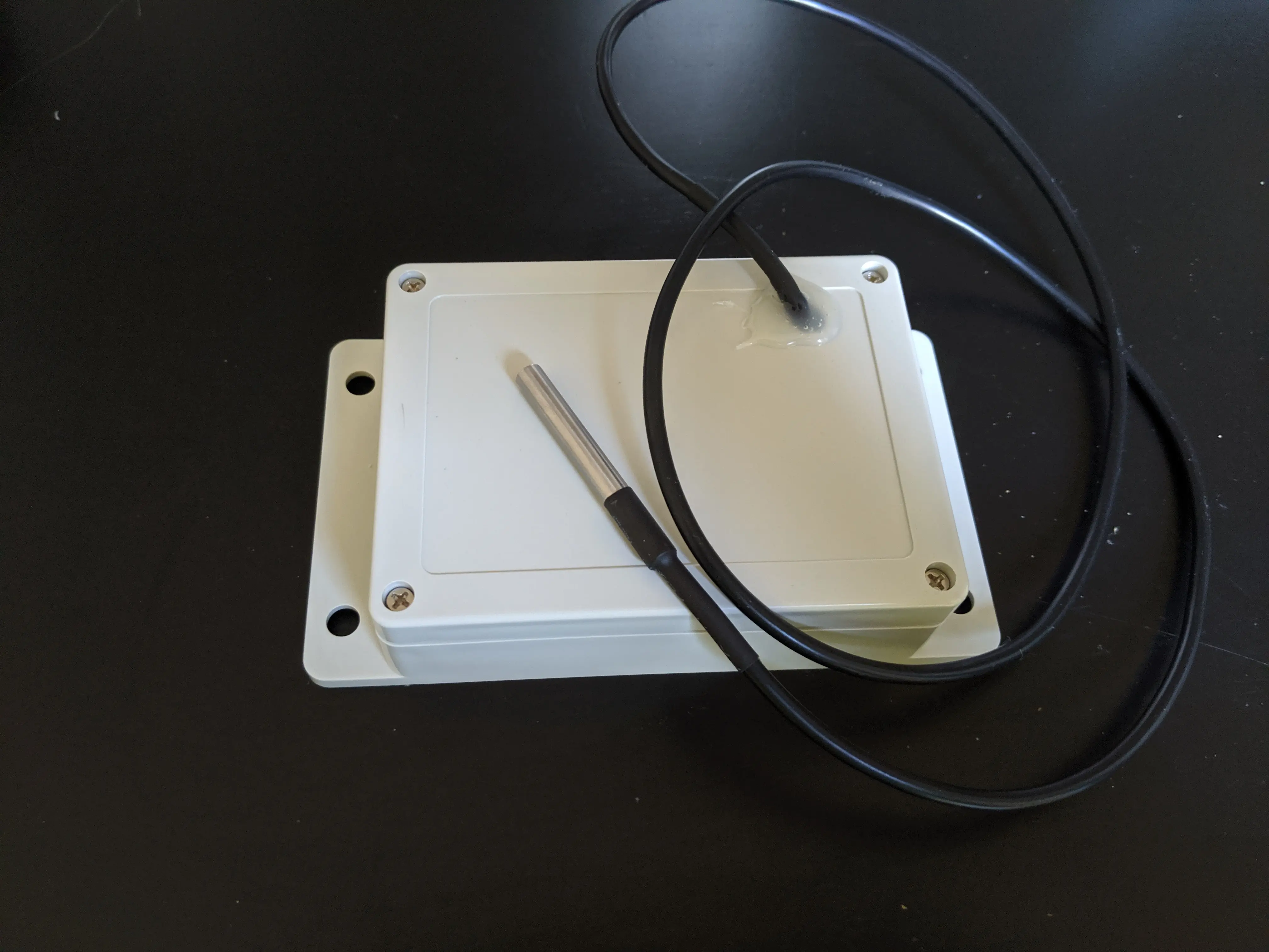 A closed electronics enclosure  box with a black temperature sensor cord coming out of it